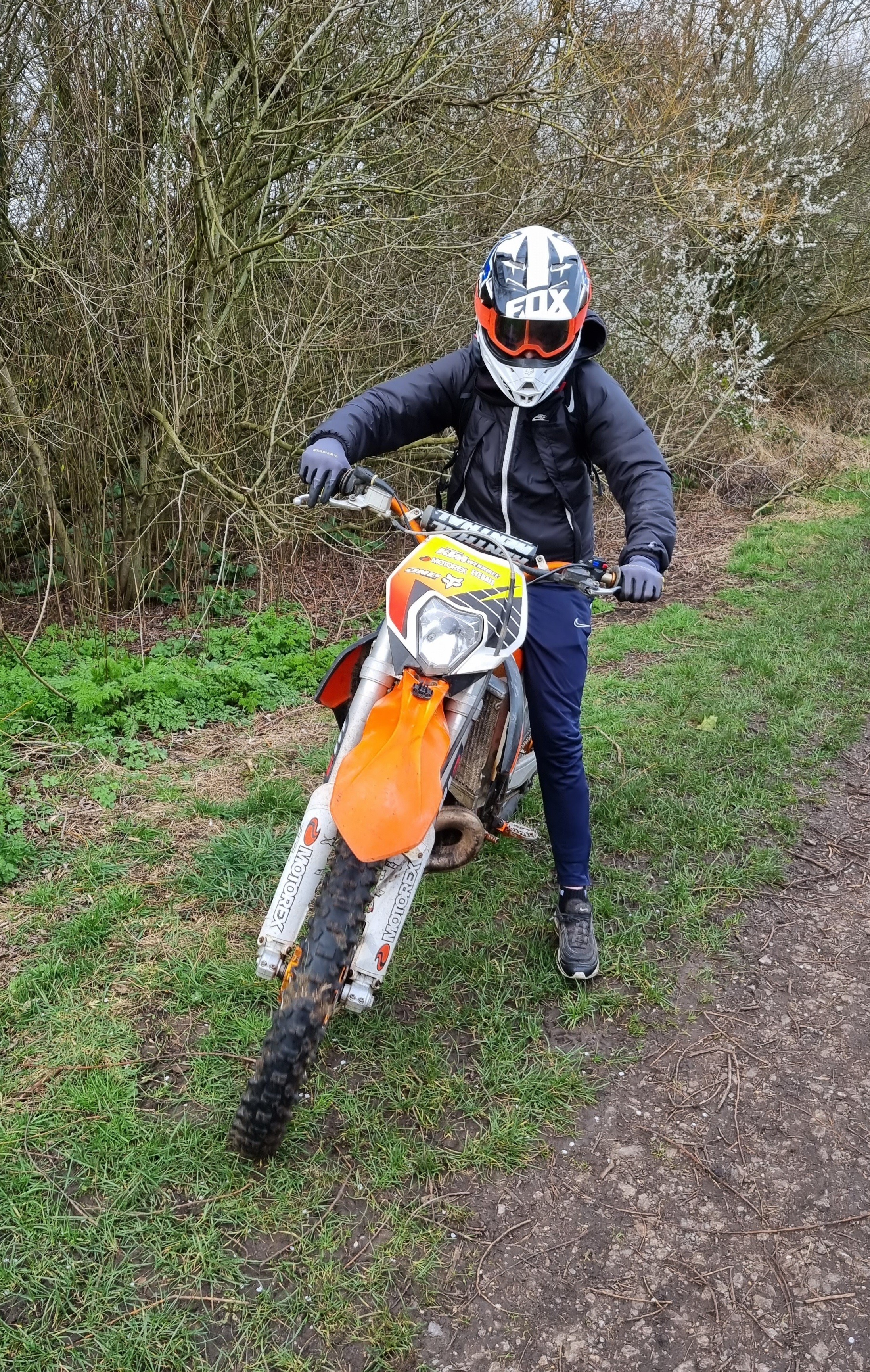 Image of off road biker sat on an orange and white bike with black clothes and a helmet on